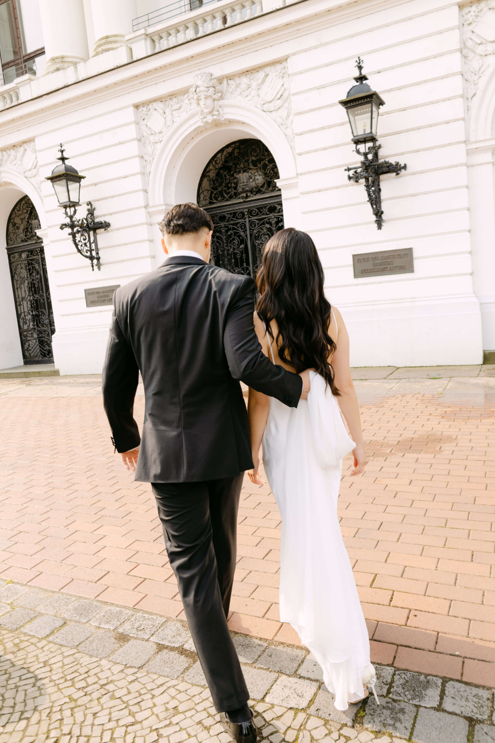 Der Bräutigam trägt die Schleppe des Brautkleides vor dem Standesamt Altona nach der standesamtlichen Hochzeit in Hamburg Altona